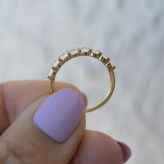 a woman's hand holding a gold ring with three stones on the side and a light purple nail polish