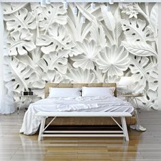 a bed sitting in front of a white wall with flowers on it's headboard