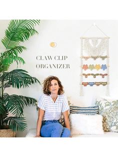 a woman sitting on a bench in front of a wall hanging with jewelry and plants