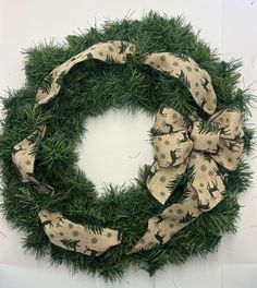 a green wreath with deers and pine needles tied to it, sitting on a white surface