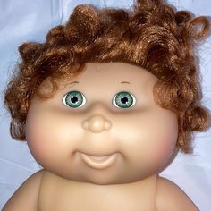 a close up of a doll with curly hair and green eyes on a white background