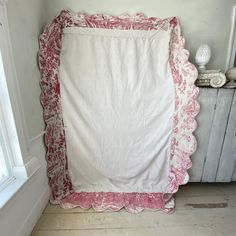 a white and pink blanket sitting on top of a wooden floor next to a window