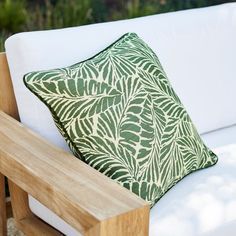 a green and white pillow sitting on top of a wooden bench next to a plant