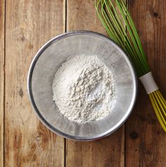 a metal bowl filled with dry ingredients next to a whisk on top of a wooden table