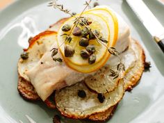 a white plate topped with meat covered in orange slices and garnished with herbs