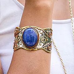 Gemstone cuff bracelet with a LAPIS LAZULLI bezel-set oval center stone. Mixed metal cuff of hammered stainless steel, accented with copper & brass motifs. Each stone is unique and varies in size & color. The Stainless Steel base makes it hypoallergenic for those with sensitive skin. These cuffs are on the chunky size which may not be ideal for smaller wrists. Sizing runs about 7 inches from edge to edge with some adjustability both ways. Width: 1.75 Inches Length: 7 Inches Materials: Brass, Cop Gemstone Cuff Bracelet, Statement Cuff Bracelet, Mixed Metals, Bezel Setting, Lapis Lazuli, Cuff Bracelet, Sensitive Skin, Copper, Cuff