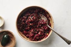 a wooden bowl filled with cranberry sauce next to two spoons on a white surface