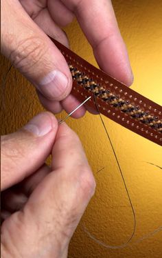 two hands are working on a piece of leather with thread and needle in the foreground