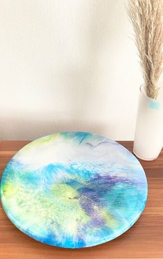 a blue and green plate sitting on top of a wooden table next to a vase