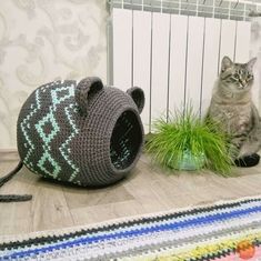 a cat sitting on the floor next to a crocheted mouse and grass plant