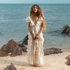 a woman standing on top of a sandy beach next to the ocean wearing a white dress