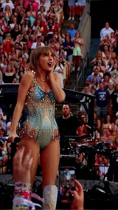 a woman in a blue and gold bodysuit talking on a cell phone at a concert