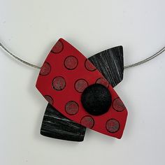 a red and black piece of art hanging from a silver chain on a white surface