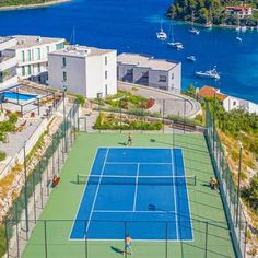 an aerial view of a tennis court in front of some buildings with boats on the water