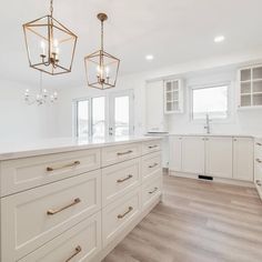 an empty kitchen with white cabinets and wood flooring is pictured in this image, there are two chandeliers hanging from the ceiling