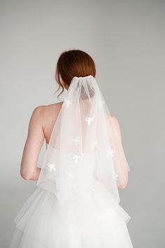 the back of a woman wearing a white veil with flowers on it's head