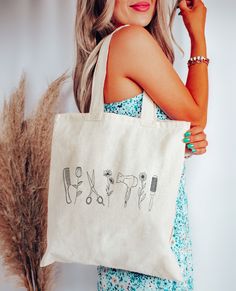 a woman is holding a tote bag with scissors and hairbrushes on it