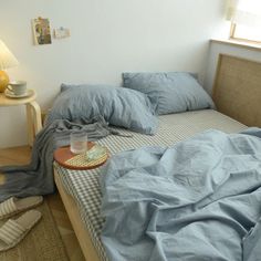 an unmade bed with blue sheets and blankets on it, next to a lamp