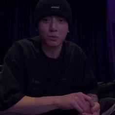 a young man sitting in front of a laptop computer wearing a beanie hat and holding a remote control