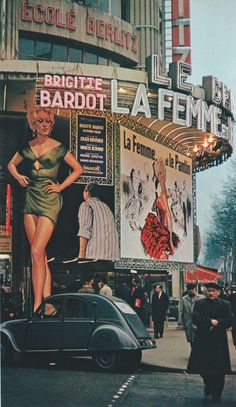 an old photo of a woman standing on the side of a building in front of a movie theater