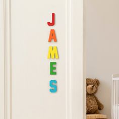 the name james is spelled in multi - colored letters on a wall next to a teddy bear