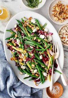 a white plate topped with green beans, red cabbage and almonds next to a bowl of nuts