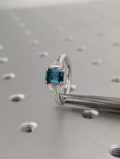 an engagement ring with a blue topazte surrounded by small white diamonds on a silver surface