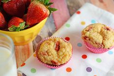 three strawberry muffins sitting on top of a table next to a bowl of strawberries