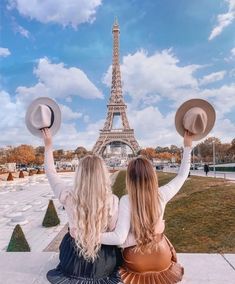 two women sitting in front of the eiffel tower with hats on their heads