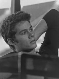 black and white photograph of a young man leaning against a wall with his hand on his head