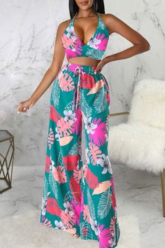 a woman standing in front of a marble wall wearing a tropical print halter top and wide legged pants