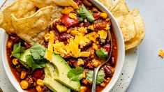 a white bowl filled with chili, corn and tortilla chips