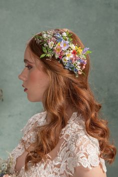 a woman with long red hair wearing a flowered headpiece and holding flowers in her hand