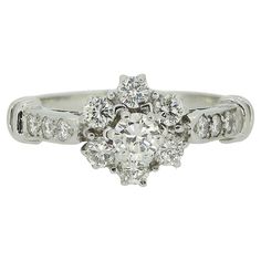 Here we have a beautiful diamond cluster ring. This vintage piece has been crafted from 18ct white and showcases a single, slightly risen round brilliant cut diamond at the centre of the face. This principal stone is then circulated by a backdrop of slightly smaller matching diamonds. Completing the ring is a ribbed shoulder design where we also find a trio of additional round brilliant cut diamonds on either side. Condition: Used (Very Good) Weight: 3.7 grams Ring Size: J (49) Band Width: 2mm F Classic Cluster Ring With Brilliant Cut Round Stone, Classic Cluster Ring For Wedding, Classic Cubic Zirconia Cluster Ring With Diamond Accents, Classic Vvs Clarity Cluster Ring, Timeless Diamond White Brilliant Cut Cluster Ring, Classic Anniversary Cluster Ring With Round Stone, Classic White Cluster Ring With Prong Setting, Anniversary Classic Cluster Ring With Round Stone, Timeless Diamond White Cluster Ring With Brilliant Cut