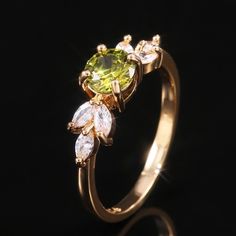 a gold ring with green and white stones on the side, against a black background