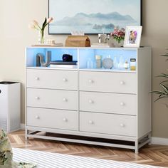 a white dresser sitting in a living room next to a plant and painting on the wall