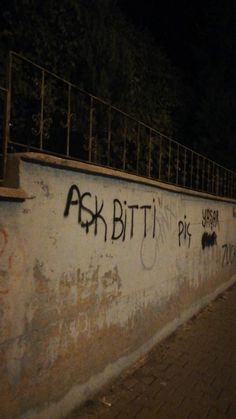 graffiti is spray painted on the side of a concrete wall at night, along with an iron fence