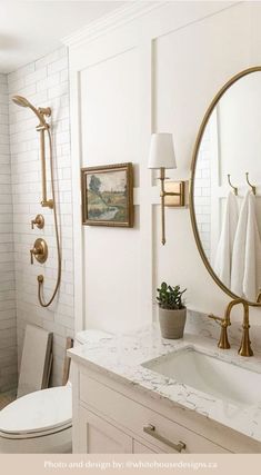 a white bathroom with gold fixtures and marble counter tops, along with a round mirror