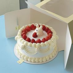 a white cake with strawberries in the shape of a bunny on top and a box behind it