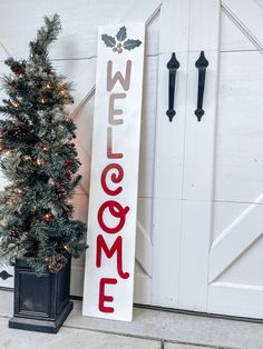 a welcome sign next to a small christmas tree in front of a white barn door