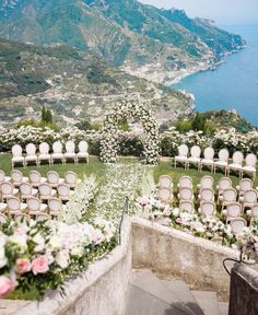 an outdoor ceremony set up with white chairs and flowers on the grass, overlooking the ocean