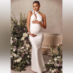 a pregnant woman standing in front of flowers wearing a white gown with halter neck