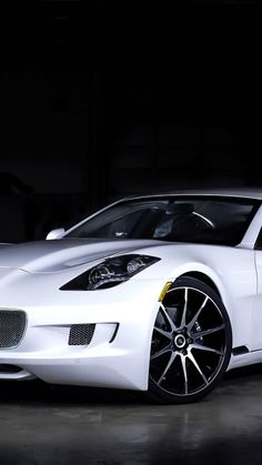 a white sports car is parked in a dark room with its hood up and lights on