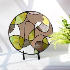 a round stained glass mirror sitting next to a potted plant