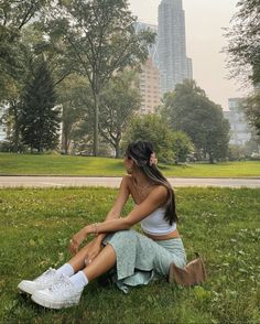 a woman sitting on the grass in front of a tall building with her legs crossed