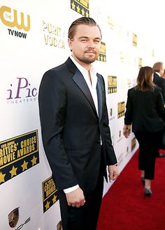 a man in a suit and tie standing on a red carpet at an awards event