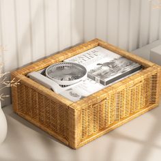 a wicker basket with magazines in it sitting on a table next to a vase