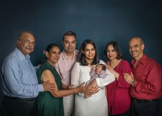 a group of people standing next to each other in front of a blue wall holding a baby