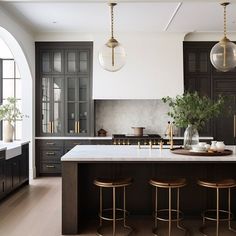 a large kitchen with black cabinets and marble counter tops, gold stools and pendant lights