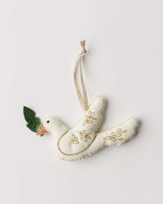 a white ornament with a green leaf on the top and an embroidered bird hanging from it's side